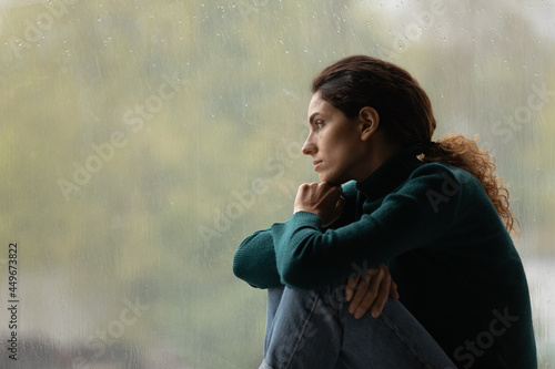 Side view frustrated thoughtful woman looking out rainy window in distance alone, lost in thoughts, upset unhappy young female feeling lonely and depressed, thinking about relationship problems photo