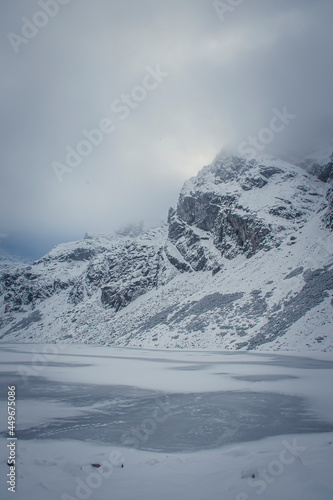 Czarny Staw Gąsienicowy Lake in winter, High Tatra Mountains, Poland. Kościelec Peak in the fog and clouds. Selective focus on the rocks, blurred background. © juste.dcv