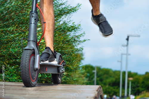 Close Up Of Man Legs Riding Electric Kick Scooter At Beautiful Park And Rising Foot. photo