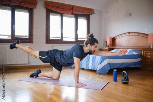 Sporty man with beard and bun hairstyle training at home.