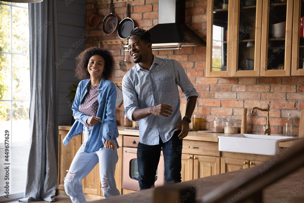 Excited millennial African American man and woman have fun dance together in home kitchen. Smiling young ethnic couple renters enjoy relocation moving to new house. Rental, real estate concept.