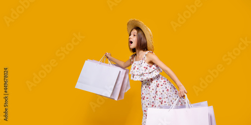 Portrait Of Joyful Teen Girl In Straw Hat With Bright Shopping Bags Over Yellow Background, Copy Space