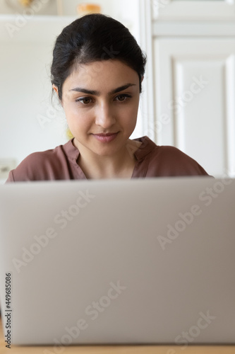 Close up narrow view of Indian young woman use laptop work or study online at home office. Ethnic female look at computer screen talk speak on video or webcam digital call. Technology concept.