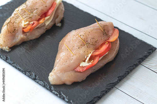 Raw chicken meat cooking with tomatoes,herbs and cheese on black slate board. Chicken fillet. Homemade recipe cook.