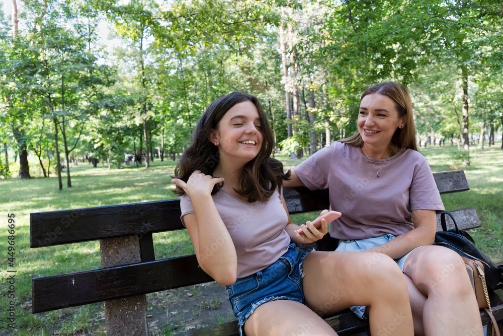 © hannamartysheva - Mom and her teenage daughter have fun laughing on a walk in a summer park. Using a smartphone © hannamartysheva - Mom and her teenage daughter have fun laughing on a walk in a summer park. Using a smartphone