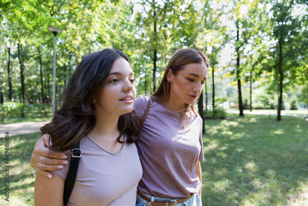 Mom and teenage daughter take a walk in the summer park. Using a smartphone