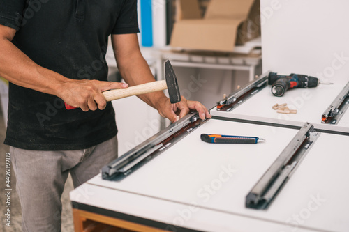Man fixing a rail on a piece of furniture with a hammer in a workshop
