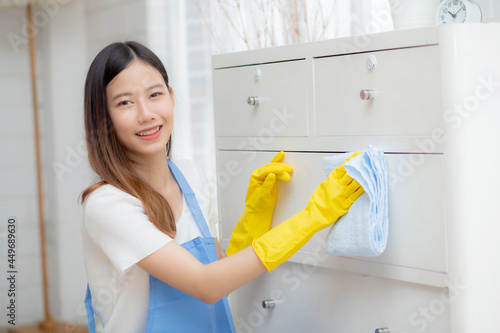 Young asian woman in gloves cleaning home in room, housekeeper is wipe with fabric, housemaid and service, worker polish dust at living room in house, housework and domestic, lifestyle concept.