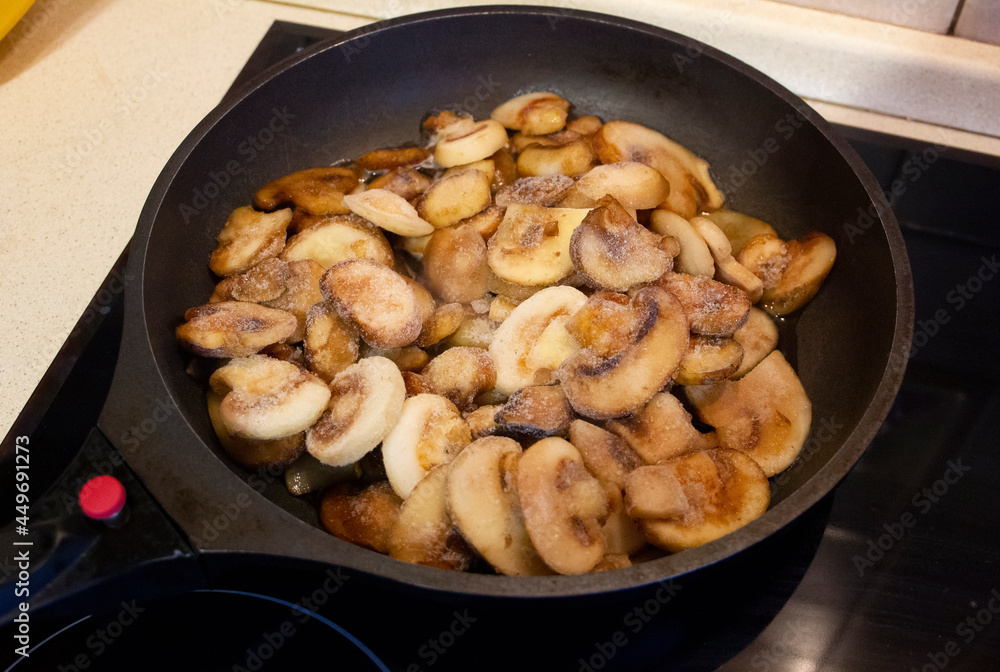 Sliced frozen mushrooms are fried in a frying pan