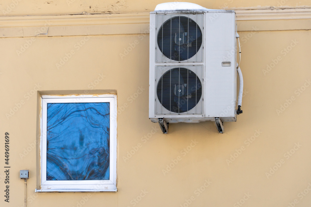 An outdoor air conditioner unit installed on the wall of a residential building next to the window. Installation, repair and maintenance of air conditioning systems in residential premises. An outdoor air conditioner unit installed on the wall of a residential building next to the window. Installation, repair and maintenance of air conditioning systems in residential premises.