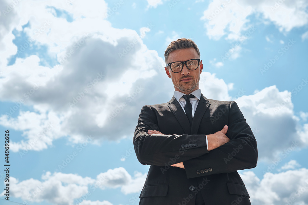 Low angle view of confident mature man in full suit keeping arms crossed Low angle view of confident mature man in full suit keeping arms crossed