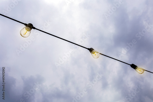 Glowing Light bulbs hanging against the dark evening sky, in a row modern decoration with copy space