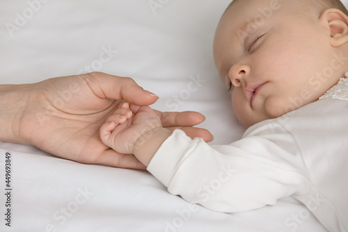 Crop close up of loving mom hold little newborn son or daughter hand sleep daydream in bedroom at home. Caring mother caress lull small baby infant child nap in bed. Motherhood, parenthood concept.