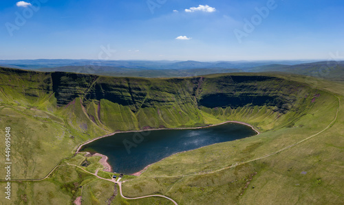 Aerial view of a lake formed at the base of green mountains (Llyn y Fan Fach, Brecon Beacons, Wales)