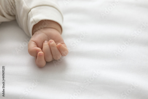 Crop close up of cute tiny fist hand of little newborn kid sleeping on white sheets in cozy bedroom. Small baby infant child nap relax in comfortable bedroom at home. Motherhood, ivf concept. photo