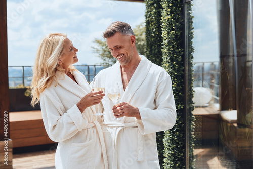 Beautiful mature couple in bathrobes enjoying champagne while relaxing in luxury hotel outdoors photo