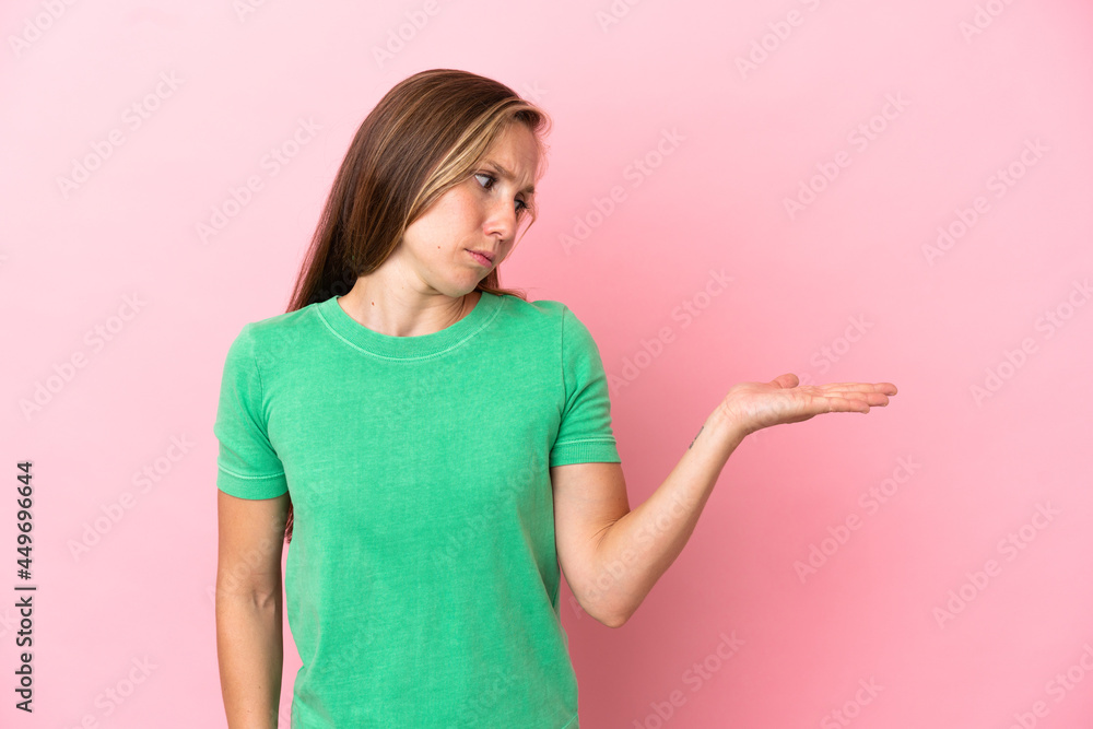 Young English woman isolated on pink background holding copyspace with doubts Young English woman isolated on pink background holding copyspace with doubts