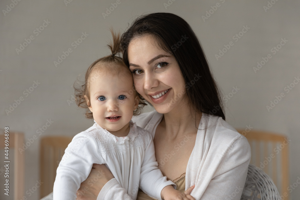 Portrait of smiling young Caucasian mother hold in arms cute little baby daughter play at home together. Happy mom hug embrace small toddler newborn kid child show love care. Motherhood concept. Portrait of smiling young Caucasian mother hold in arms cute little baby daughter play at home together. Happy mom hug embrace small toddler newborn kid child show love care. Motherhood concept.