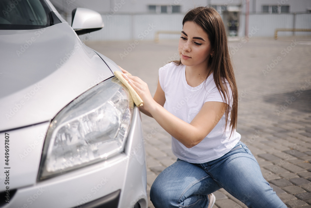 Front view of attractive happy joyful female driver washing her car's headlights with special rag in self-service car wash Front view of attractive happy joyful female driver washing her car's headlights with special rag in self-service car wash