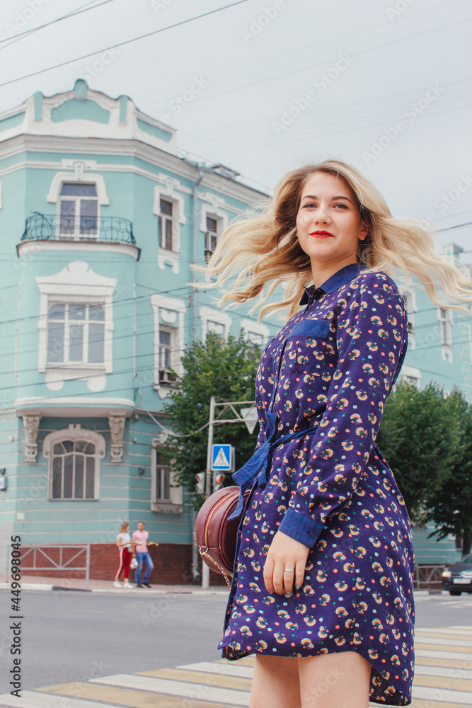 Young beautiful woman in blue dress with a round bag walking on the spring street. Urban background. Stylish Tourist girl enjoying walking the city during weekend trip.