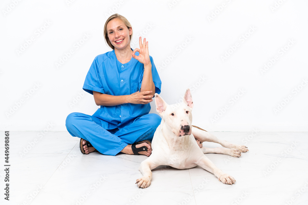 Young veterinarian English woman sitting on the floor with dog showing
