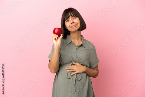 Woman over isolated background pregnant and frustrated while holding an apple