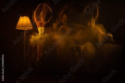 Long exposure of ballerina, dancers in movement in tutu with light on a black background. Both arms and a leg lifted up.