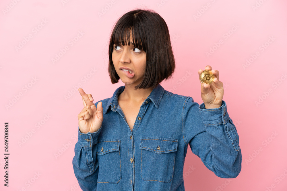 Young mixed race woman holding a Bitcoin isolated background with fingers crossing and wishing the best Young mixed race woman holding a Bitcoin isolated background with fingers crossing and wishing the best