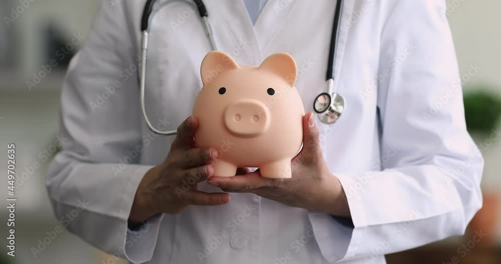 Hands of African male gp therapist in white coat holding piggy bank close up cropped view. Social medical care, free medicare for citizen, save money, special offer, health checkup in clinic concept Hands of African male gp therapist in white coat holding piggy bank close up cropped view. Social medical care, free medicare for citizen, save money, special offer, health checkup in clinic concept