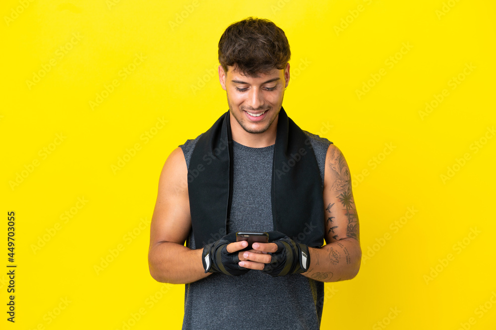 Young sport caucasian man with towel isolated on yellow background sending a message with the mobile Young sport caucasian man with towel isolated on yellow background sending a message with the mobile