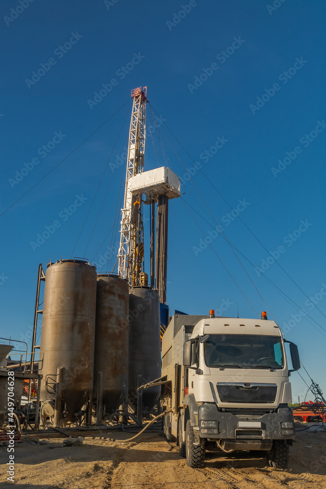 Drilling rig with well cementing equipment in the foreground. Infrastructure, communications and drilling equipment are visible. Cementing unit on a car chassis. Cement storage tanks