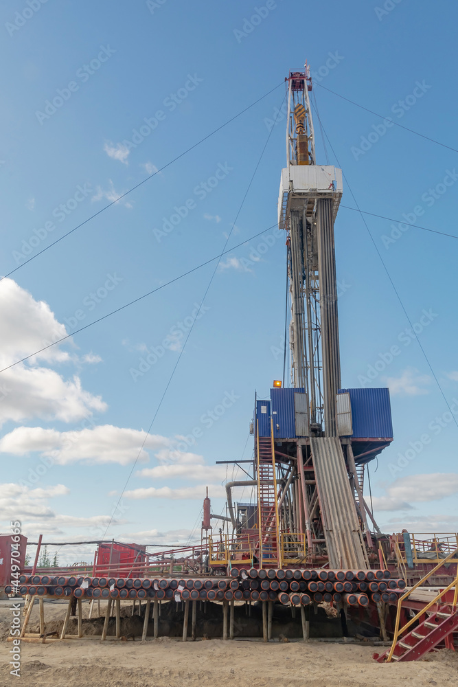 The design of a drilling rig for drilling wells in an oil and gas field in the far north. Oil rig with standing drill pipes and equipment against blue sky