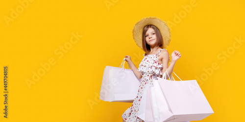 Portrait Of Joyful Teen Girl In Straw Hat With Bright Shopping Bags Over Yellow Background