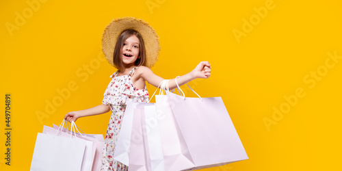 Portrait Of Joyful Teen Girl In Straw Hat With Bright Shopping Bags Over Yellow Background