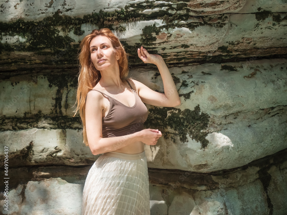 A girl stands by a smooth relief moss-covered rock on a summer sunny day A girl stands by a smooth relief moss-covered rock on a summer sunny day