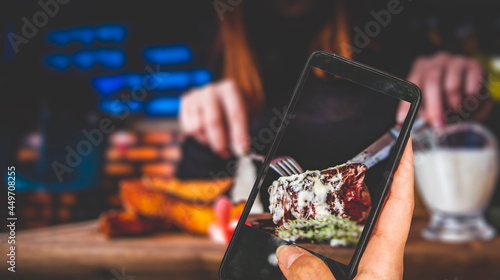 woman hand holding and showing smart phone takes a photo woman hands with fork and knife eating beef steak in cafe. food photos
