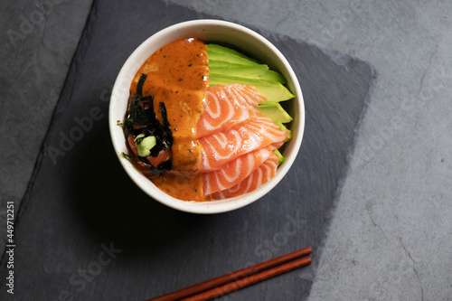 Salmon poke bowl with avocado and seaweed spicy sauce Japanese style. Top view on black table background. Asian trendy food.