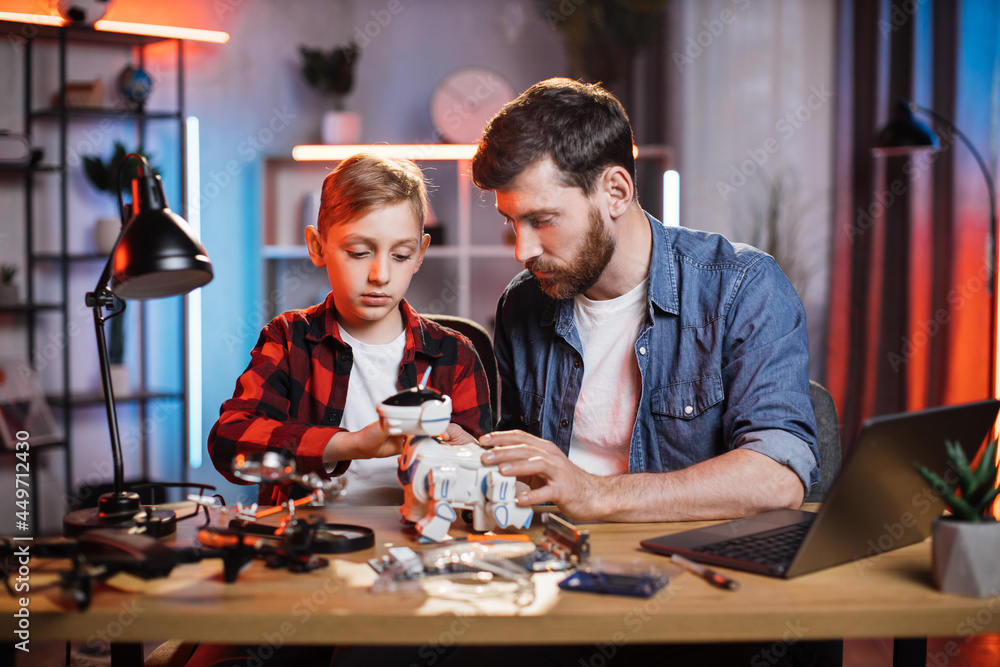 Caring father controlling repairing process of toy robot dog by his little son. Bearded man teaching boy fixing broken appliances at home. Educational moments during parenthood.