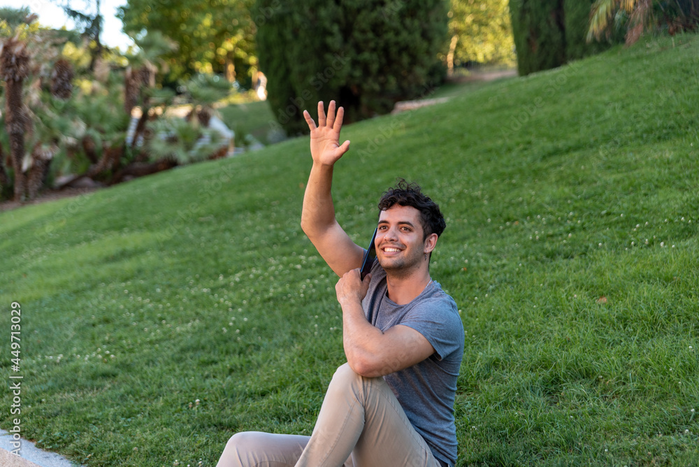 Young latin man greeting someone in the park Young latin man greeting someone in the park
