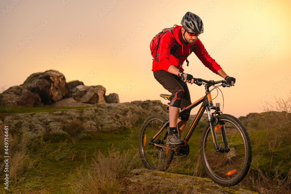 Cyclist in Red Riding Bike on the Spring Rocky Trail at Sunset. Extreme Sport and Enduro Biking Concept.