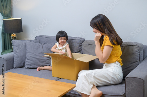 Happy mom with daughter opening cardboard box in living room at home