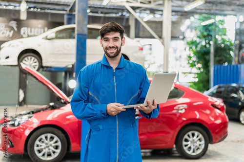 Portrait photo of professional look Caucasian vehicle service technician standing indoor of car repair shop and holding notebook computer. © pitipat