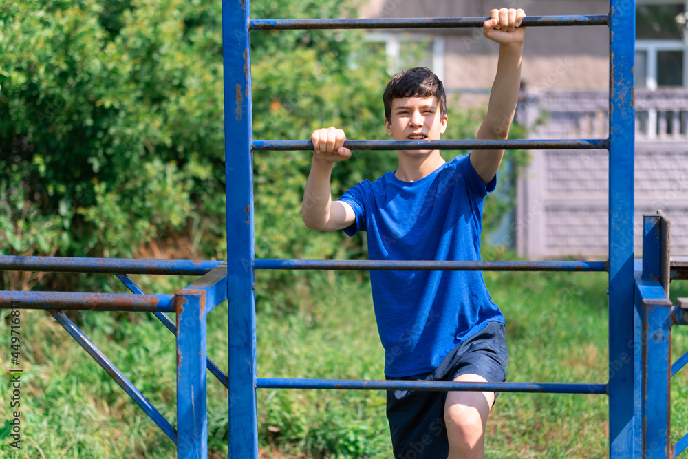 Obraz premium teenage boy exercising outdoors, sports ground in the yard, he posing at the horizontal bar, healthy lifestyle