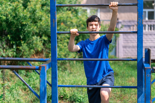 teenage boy exercising outdoors, sports ground in the yard, he posing at the horizontal bar, healthy lifestyle