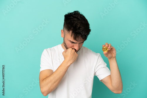 Young man holding a Bitcoin isolated on blue background having doubts
