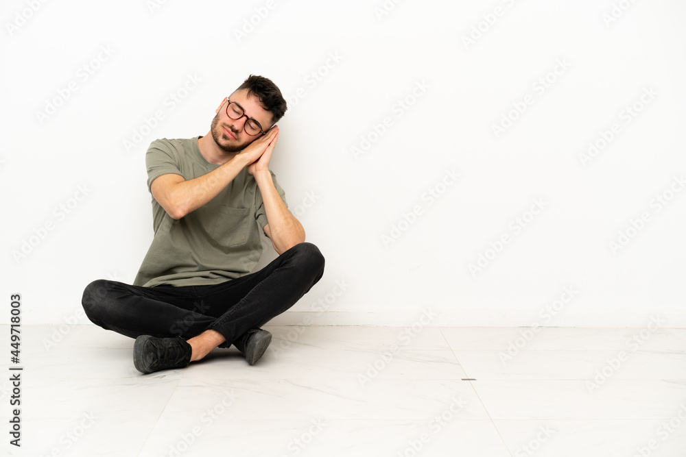 Young caucasian man sitting on the floor isolated on white background making sleep gesture in dorable expression Young caucasian man sitting on the floor isolated on white background making sleep gesture in dorable expression