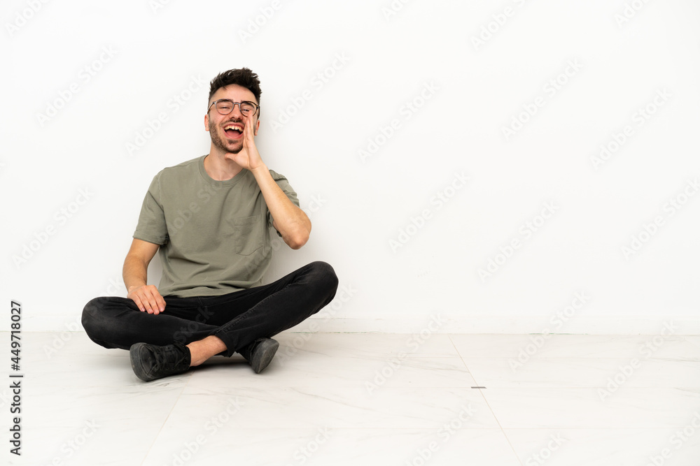 Young caucasian man sitting on the floor isolated on white background shouting with mouth wide open Young caucasian man sitting on the floor isolated on white background shouting with mouth wide open