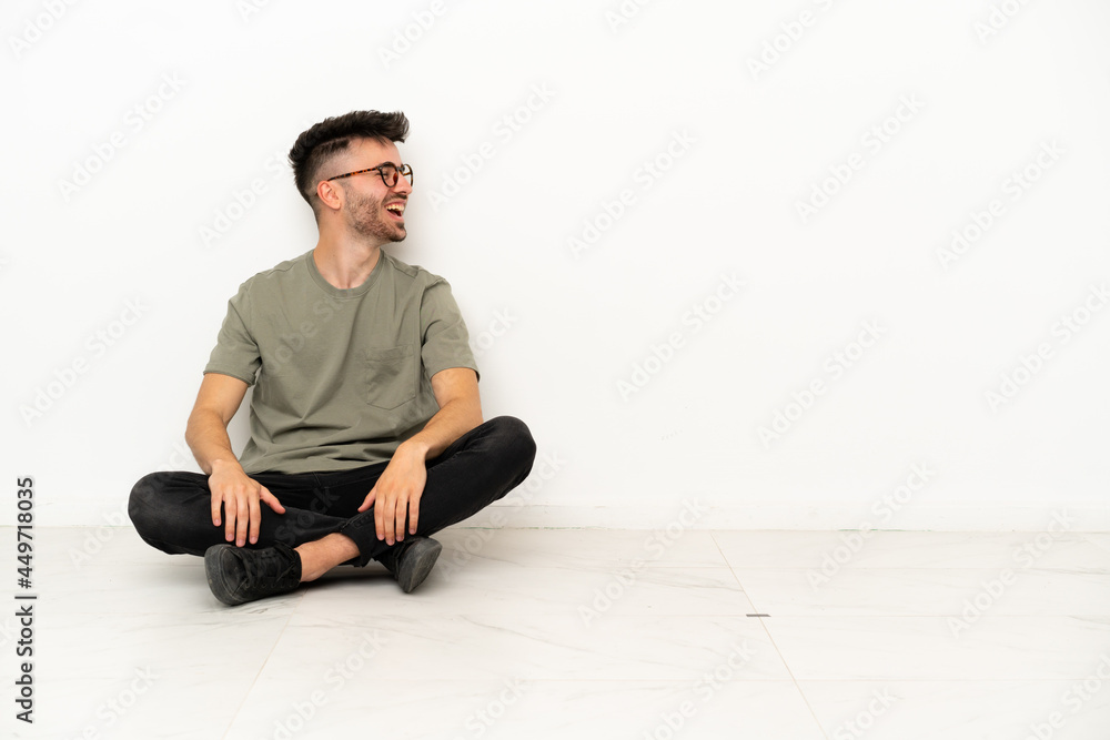 Young caucasian man sitting on the floor isolated on white background laughing in lateral position Young caucasian man sitting on the floor isolated on white background laughing in lateral position