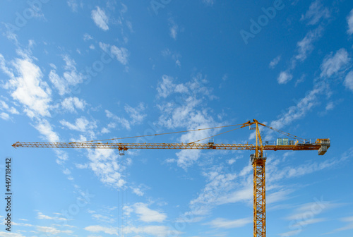 A yellow construction tower crane against a blue sky with clouds