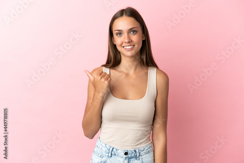 Young woman over isolated pink background pointing to the side to present a product